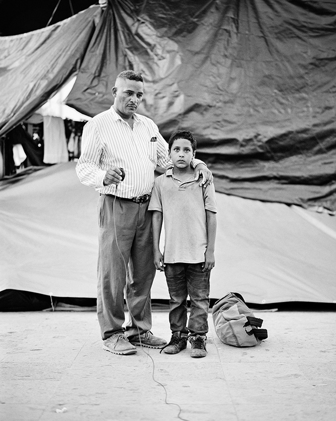 Φωτογράφος της Χρονιάς και πρώτη θέση στην κατηγορία Πορτρέτο. Ο σαραντάχρονος Εντουάρντο Μπεναβίδες και ο εννιάχρονος γιος του Τζόναθον, μετανάστες από το Ελ Σαλβαδόρ, σε άτυπο καταυλισμό στο Μεξικό. «Αυτή είναι μια σειρά από πορτρέτα που τράβηξαν μόνοι τους κάποιοι μετανάστες στο Μεξικό, καθώς περιμένουν να περάσουν τα σύνορα προς τις ΗΠΑ. Για να απαθανατίσω ένα κομμάτι αυτού του αβέβαιου ταξιδιού τοποθέτησα μια κάμερα σε ένα τρίποδο με καλώδιο και μετά έκανα πίσω, επιτρέποντας στους μετανάστες να επιλέξουν εκείνη τη στιγμή του κλικ και να τους δώσω λόγο στη διαδικασία τεκμηρίωσης της ζωής τους», γράφει ο βραβευμένος αυστραλός φωτογράφος