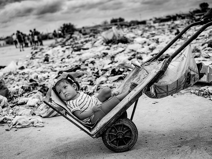 Πρώτη θέση, κατηγορία Ντοκιμαντέρ. Πατέρας μεταφέρει το κοριτσάκι του σπίτι, διασχίζοντας μια χωματερή στον εγκαταλειμμένο αεροδιάδρομο έξω από το Μαϊκάο της Κολομβίας. Περισσότεροι από 8,5 εκατομμύρια οικονομικοί μετανάστες από τη Βενεζουέλα ζουν στην περιοχή, δίχως πρόσβαση σε περίθαλψη, στέγη, καθαρό πόσιμο νερό ή φαγητό. Και όπως γίνεται αντιληπτό, τα παιδιά πληρώνουν το υψηλότερο τίμημα
